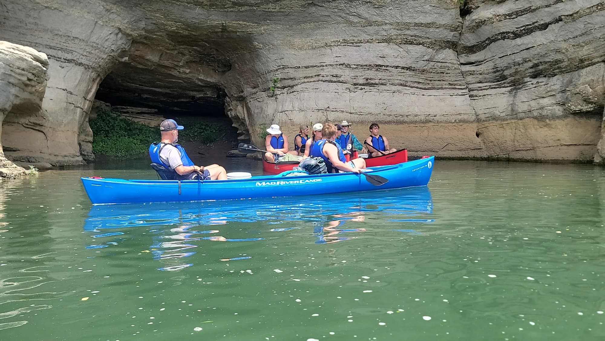 Canoes passing beneath a towering river bluff on the expedition
